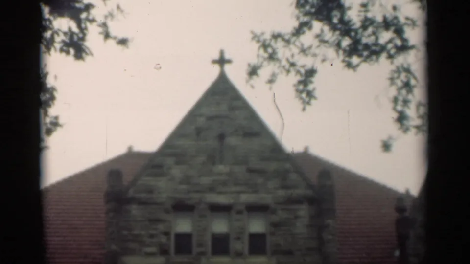 1949 New Orleans frame showing the church gable topped by a Christian cross, with roofline, upper windows, and tree branches in view.