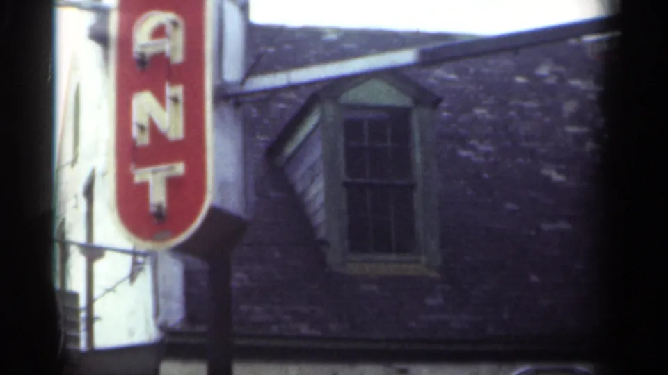 Late-1940s New Orleans street detail with a vertical red sign, brick wall, upper window, and roofline visible in soft 8mm color.