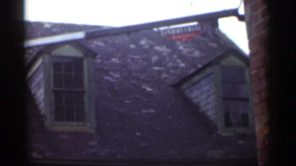 Home-movie frame from 1949 New Orleans looking up at the Marble Hall roof, dormers, brick edge, and small red roofline sign.