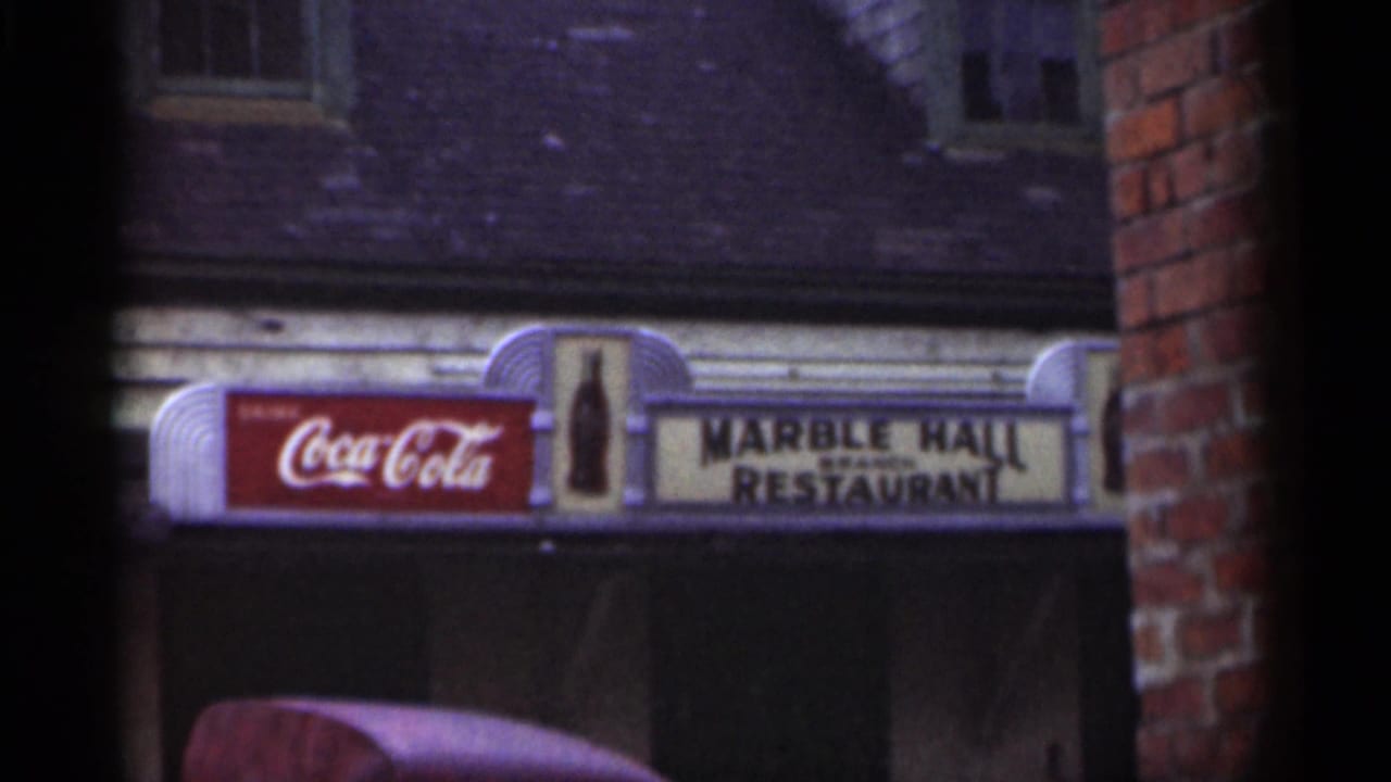 Coca-Cola sign beside Marble Hall Restaurant sign above a storefront, framed by brick.