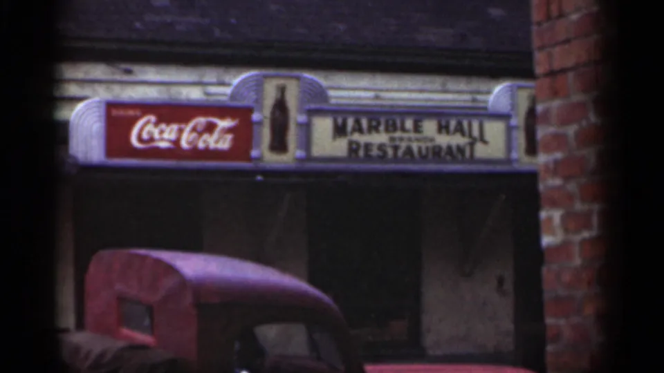 1949 New Orleans storefront view showing the Marble Hall Restaurant sign, Coca-Cola panel, brick edge, and red vehicle below.