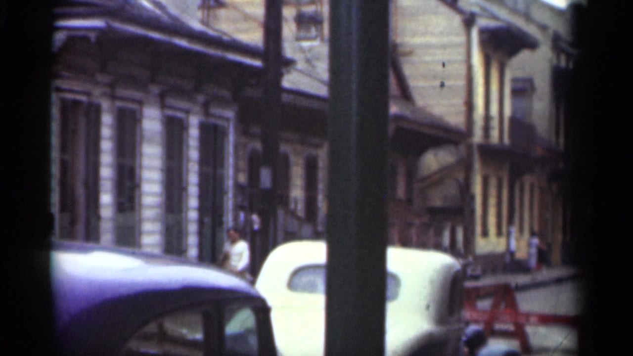 Street view with parked cars, older building fronts, a utility pole, and a pedestrian on the sidewalk.
