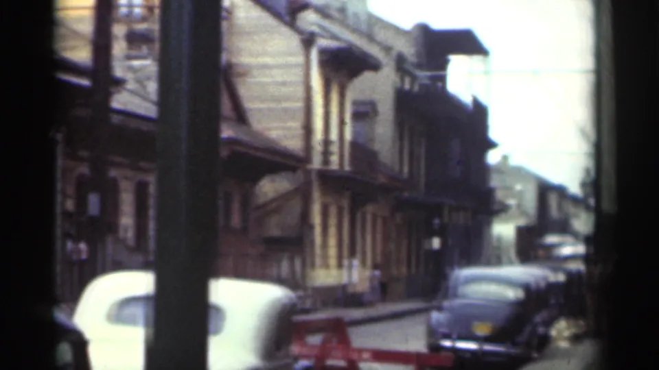 1949 New Orleans street view looking past a white car toward parked automobiles, wood-sided buildings, and a bright sky beyond.