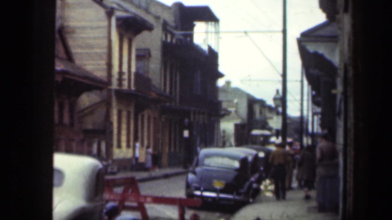 1949 New Orleans street view with classic cars parked along the curb, pedestrians on the sidewalk, and low-rise storefront buildings.