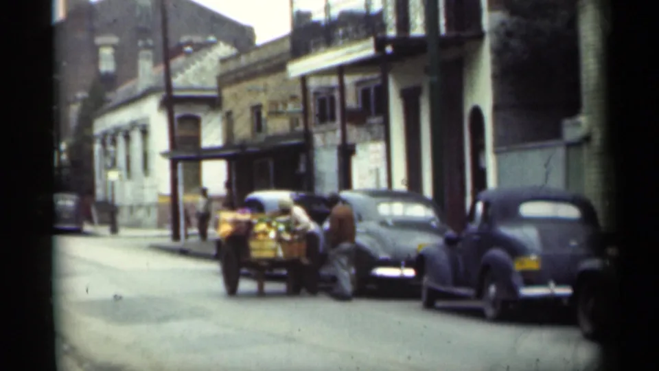 1949 New Orleans street scene showing a small loaded cart beside parked automobiles, with several people standing nearby.