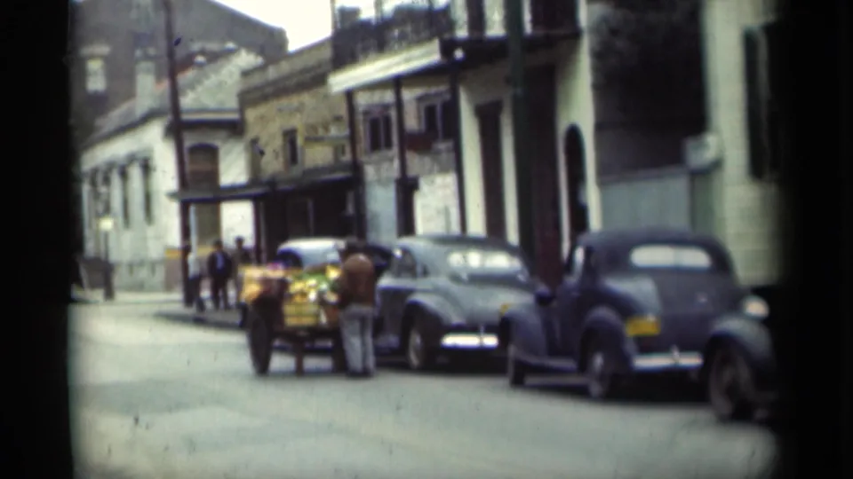 1949 New Orleans curbside scene showing pedestrians near a cart and several parked classic automobiles.