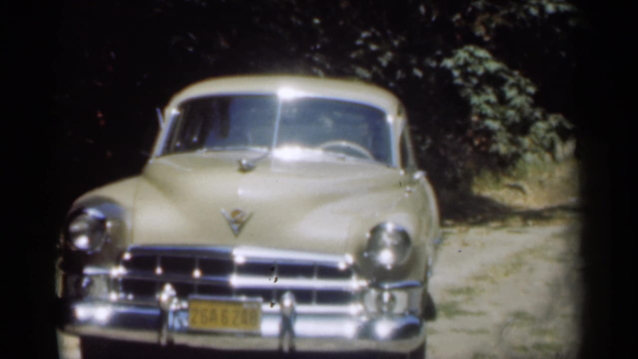 1949 New Orleans frame with a beige Buick-style automobile facing the camera, chrome bright in sunlight and trees behind it.