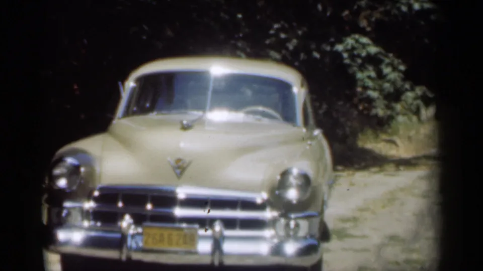 1949 New Orleans frame with a beige Buick-style automobile facing the camera, chrome bright in sunlight and trees behind it.