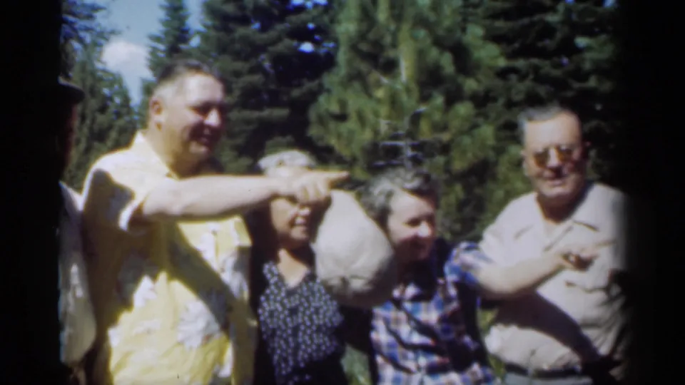 The man in the yellow patterned shirt points off-camera as the group remains gathered outdoors in 1949 New Orleans footage.