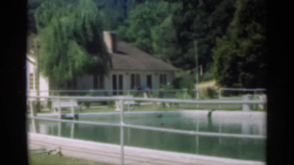 Santa Cruz 8mm still with a sloped-roof house, pond railings, trees, and muted water reflections.