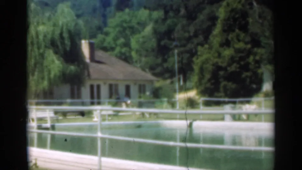 Final 1949 Santa Cruz frame with farmhouse, willow, pond or pool, white railings, wooded backdrop, and a small distant person on the grounds.