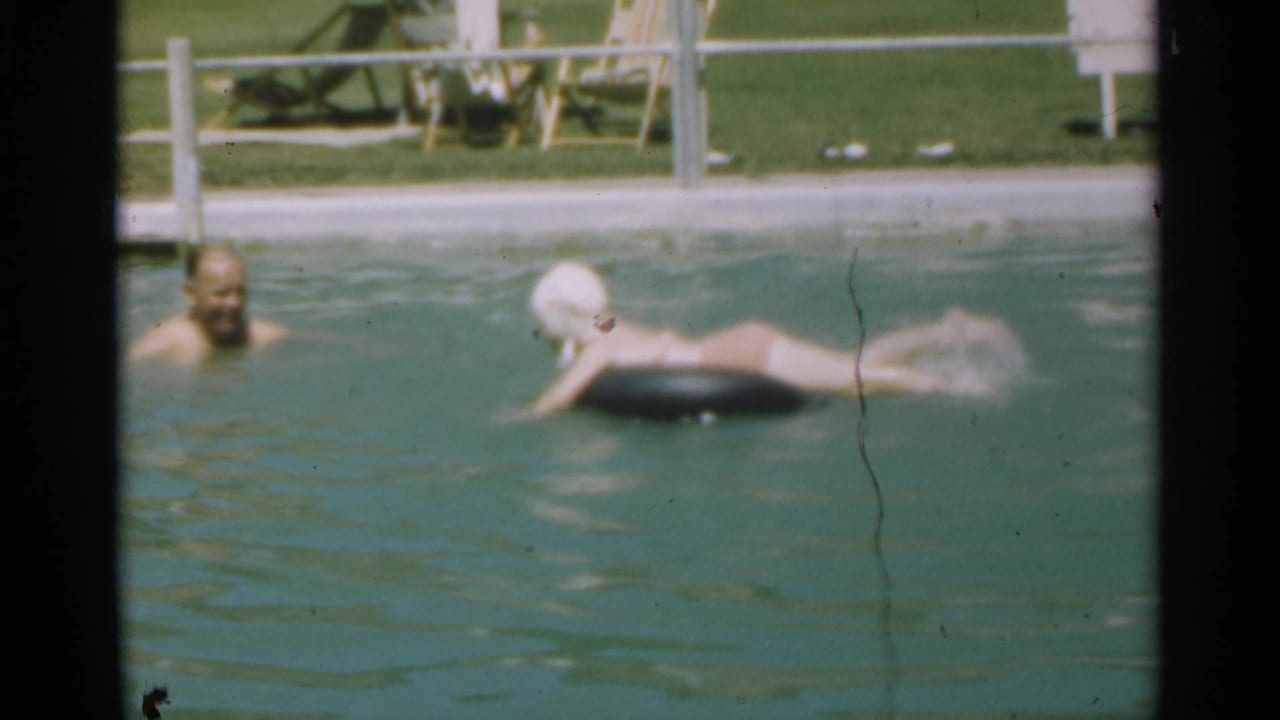 1949 Santa Cruz pool scene with a young swimmer in a white cap kicking at an inner tube as an adult looks on from nearby water.