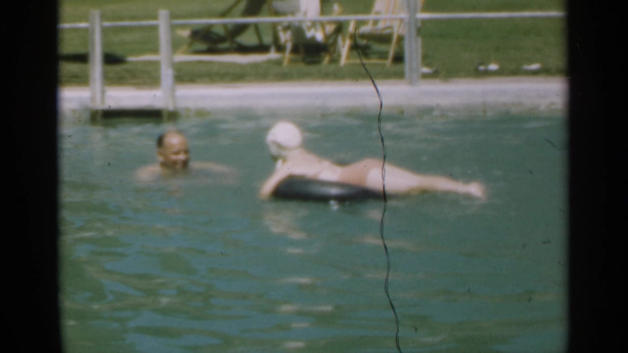 Swimmer in a white cap floats on an inner tube while a man faces her in the pool.
