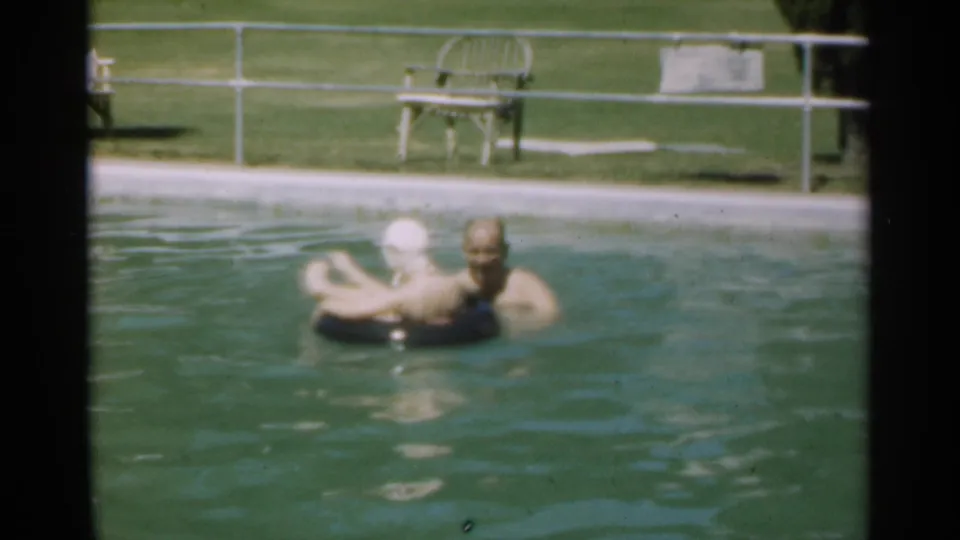 The couple gathers around the black inflatable ring in the 1949 Santa Cruz pool footage, framed by soft 8mm focus.