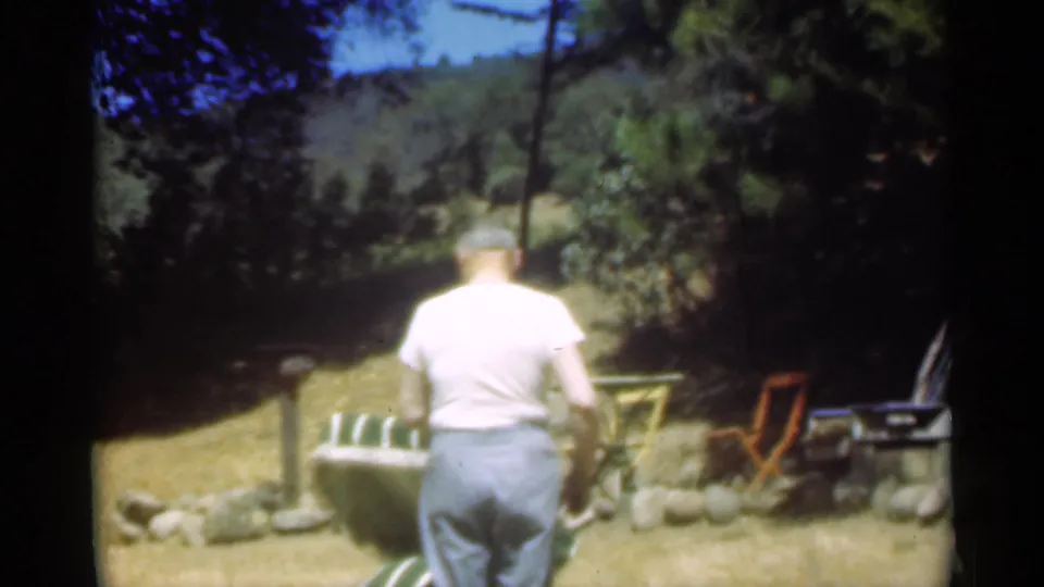 In a 1949 Santa Cruz backyard scene, a man stands with his back to the camera beside a green and white striped lawn chair.