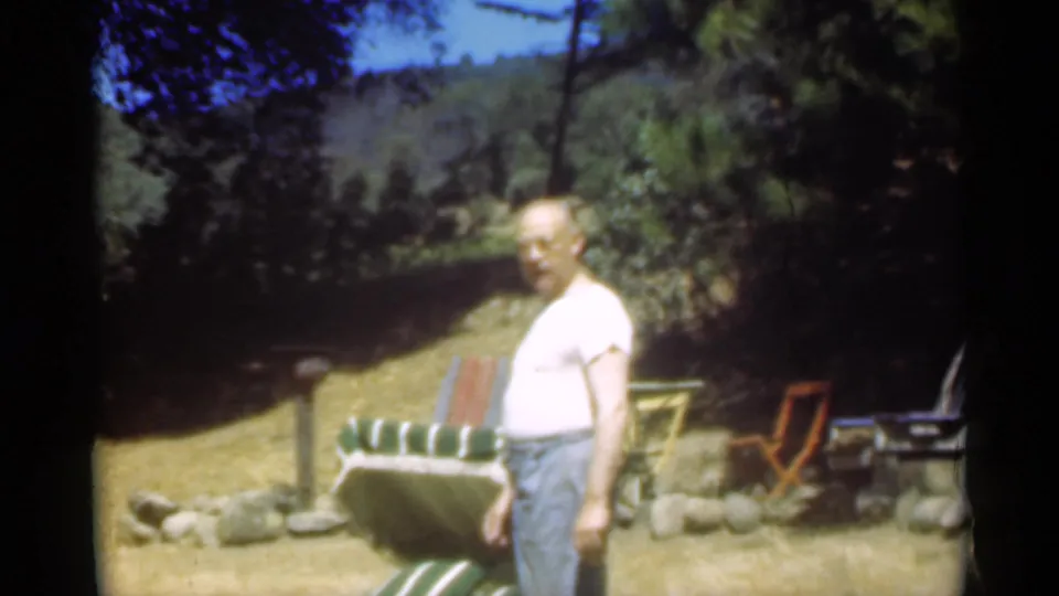 The man turns toward the camera beside the green and white striped chair in the 1949 Santa Cruz backyard footage.