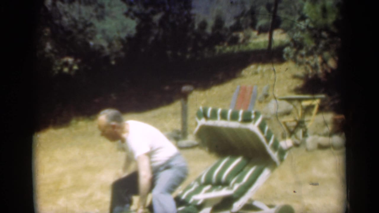 Man bends beside a green and white striped reclining lawn chair.