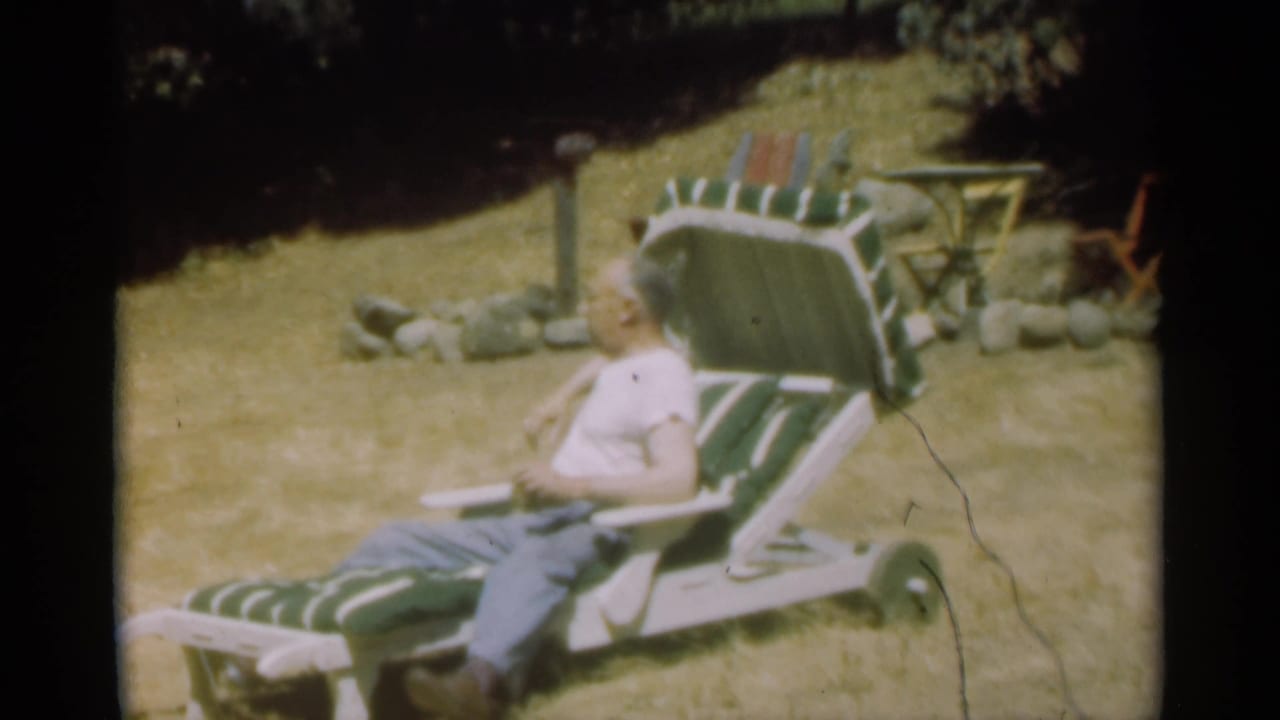 Man reclining on a striped lawn chair in a grassy yard.