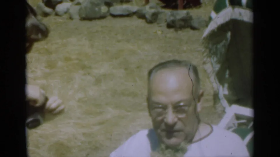 An older man in glasses faces the home-movie camera in the Santa Cruz outdoor setting, with grass and rocks behind him.