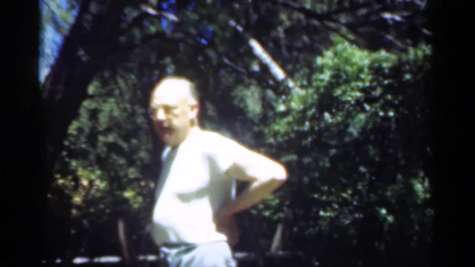 In supported 1949 Santa Cruz home-movie footage, a man stands among trees with hands on hips in dappled sunlight.