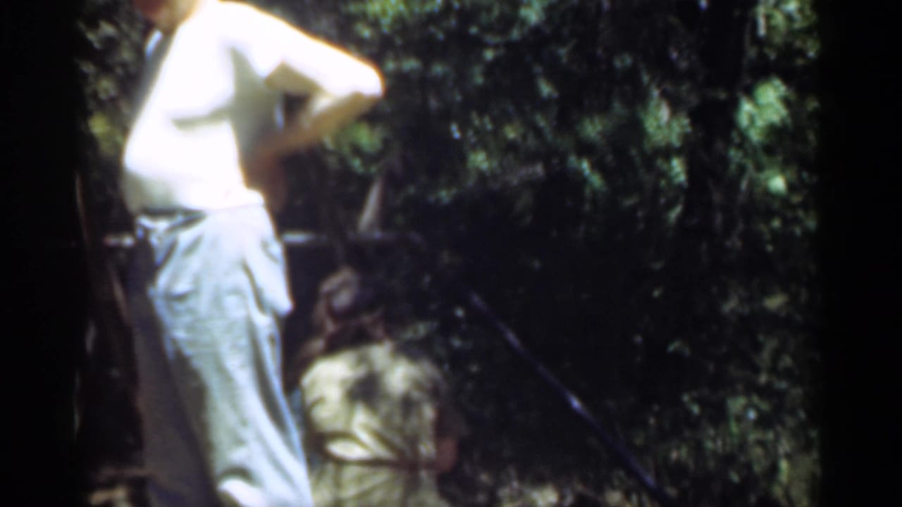 The 1949 Santa Cruz frame shows the standing man in profile near dense trees, with another person crouched in the background.