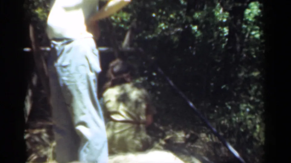 A cropped view from the Santa Cruz home movie shows the man standing near a tree, with a crouched figure at lower right.