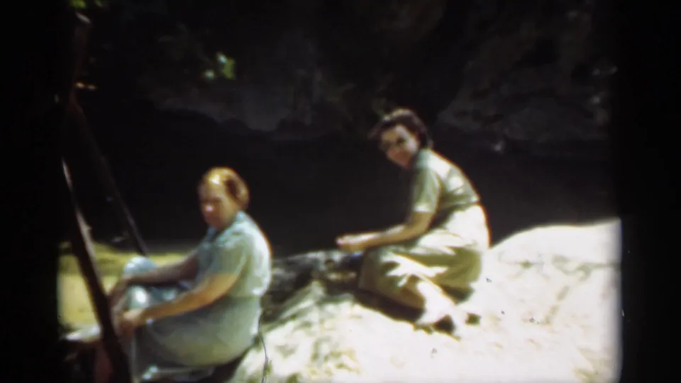 The final frame shows the two women still seated beside shaded water in Santa Cruz, with an easel-like object at left and sunlit rock below.