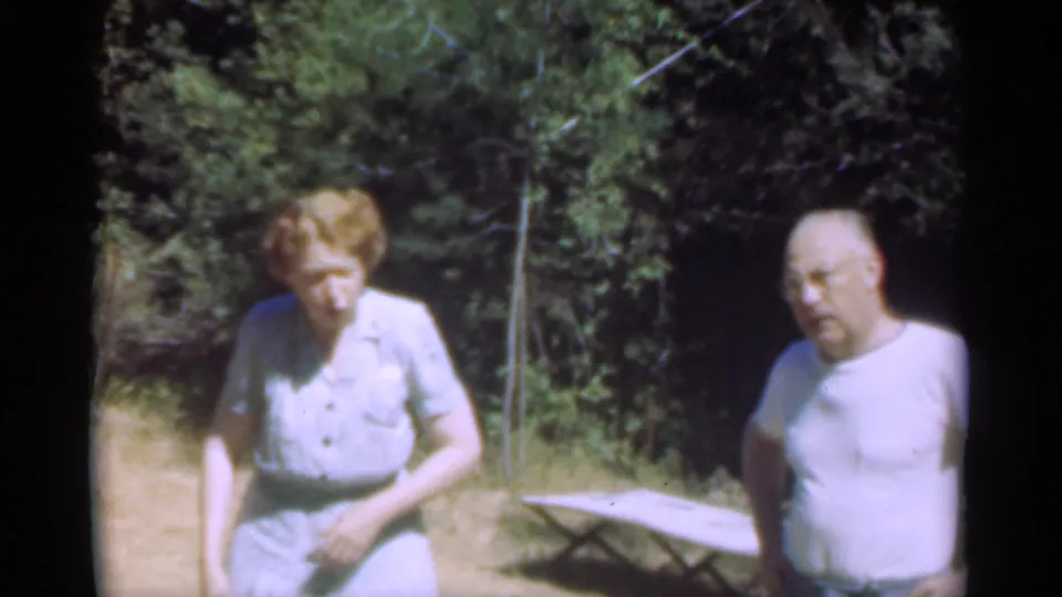 Adults in a wooded vacation setting, one woman in a light dress and a man in a white shirt, from the 1949 home movie.