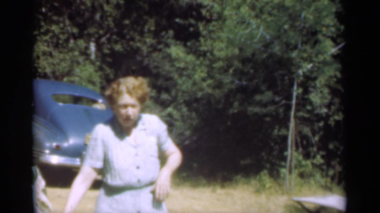 Woman faces forward near a parked blue car with trees behind her.
