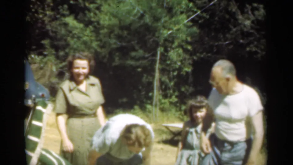 A woman in green smiles while another adult bends toward a child and a man stands nearby in the Santa Cruz home-movie scene.