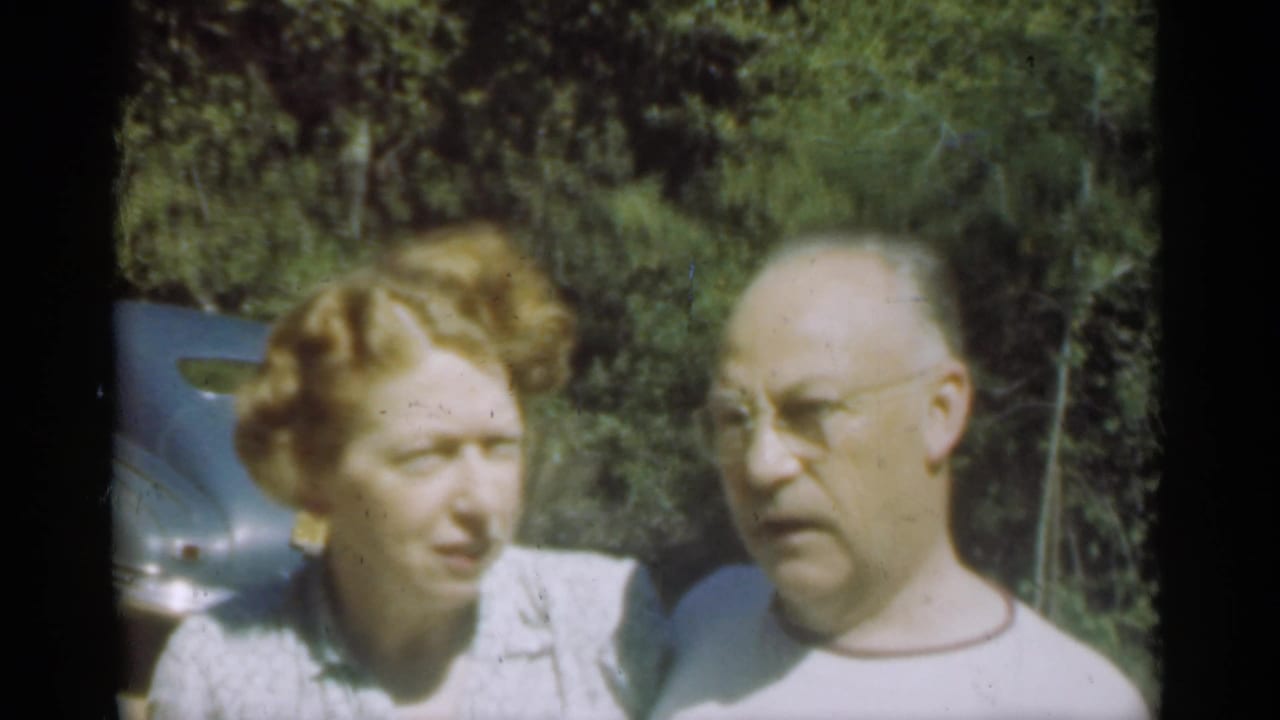 Woman turns toward a man as they stand beside a blue car outdoors.