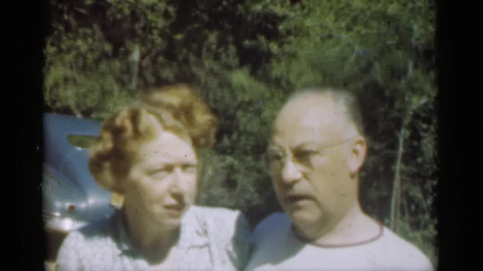 The woman turns toward the man during a casual 1949 Santa Cruz home-movie moment beside a blue car and trees.