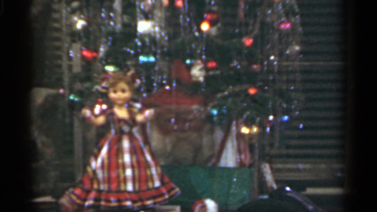 Decorated Christmas tree with tinsel, colored lights and a plaid-dressed doll in front.