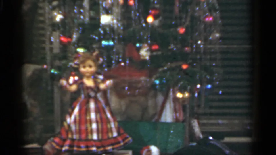 1949 Santa Cruz home-movie frame showing a tinsel-covered Christmas tree with colored lights and a doll in a plaid dress near the foreground.