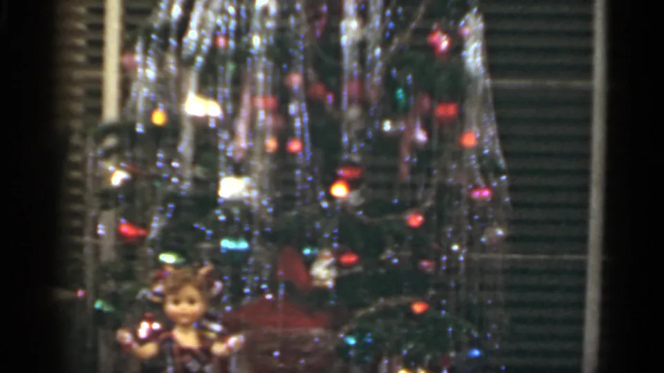 1949 Santa Cruz home-movie frame emphasizing tinsel, colored ornaments and lights, with the doll visible near the bottom edge.