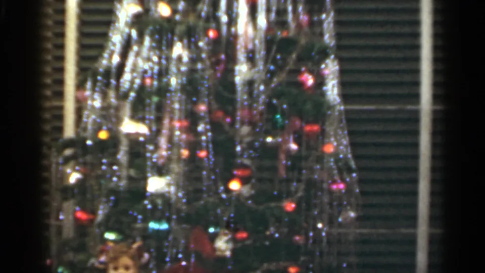 1949 Santa Cruz home-movie frame showing a close view of a Christmas tree with tinsel, colored lights, ornaments and shutters behind it.