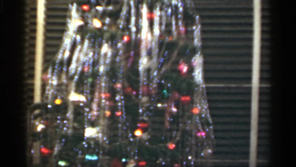 Close 1949 Santa Cruz home-movie view of a Christmas tree with shiny tinsel, colored bulbs, and ornaments behind window blinds.
