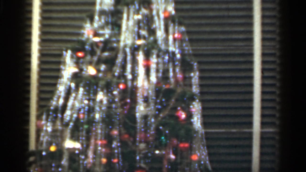 1949 Santa Cruz holiday tree detail showing dense tinsel, small colored bulbs, ornaments, and the striped backdrop of closed blinds.