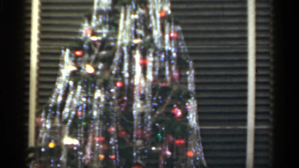 1949 Santa Cruz holiday tree detail showing dense tinsel, small colored bulbs, ornaments, and the striped backdrop of closed blinds.