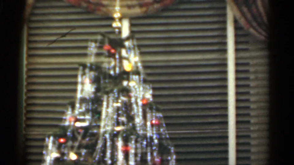 1949 Santa Cruz home-movie still of the upper Christmas tree, with tinsel, ornaments, colored bulbs, and window blinds in the background.