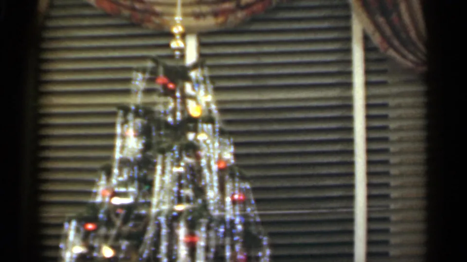 1949 Santa Cruz home-movie frame showing a decorated Christmas tree with tinsel, colored lights, and blinds behind it.