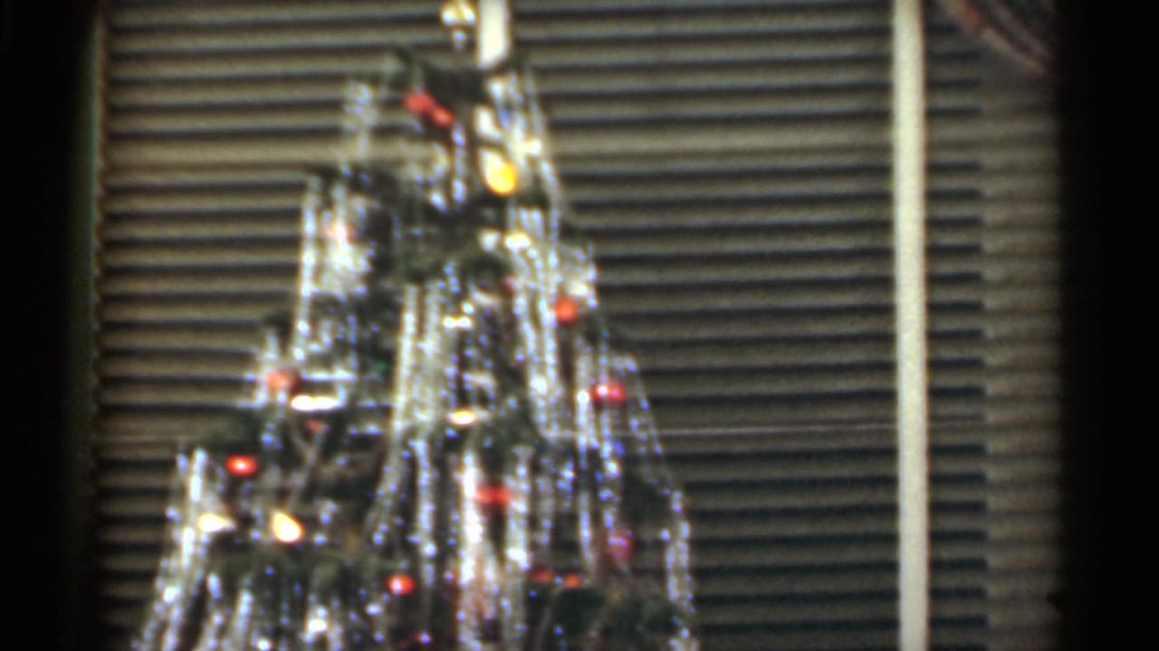 1949 Santa Cruz holiday frame with the upper Christmas tree, shiny tinsel, colored bulbs, and venetian blinds in the background.