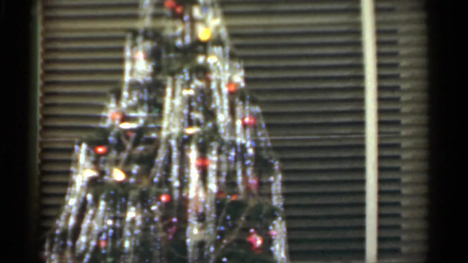 1949 Santa Cruz home-movie frame showing a fuller view of the Christmas tree, bright tinsel, red ornaments, and window blinds.