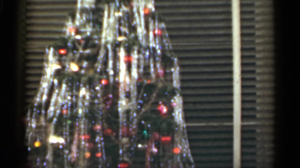 1949 Santa Cruz frame of a tinsel-heavy Christmas tree with colored lights and ornaments in a softly focused interior.