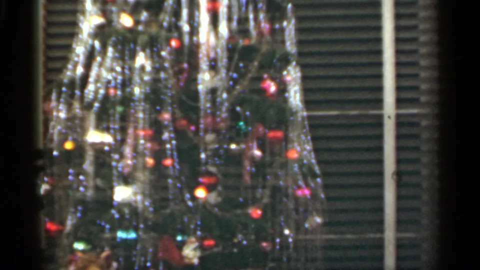 1949 Santa Cruz home-movie frame with a decorated Christmas tree, bright tinsel, colored ornaments, and window blinds behind it.