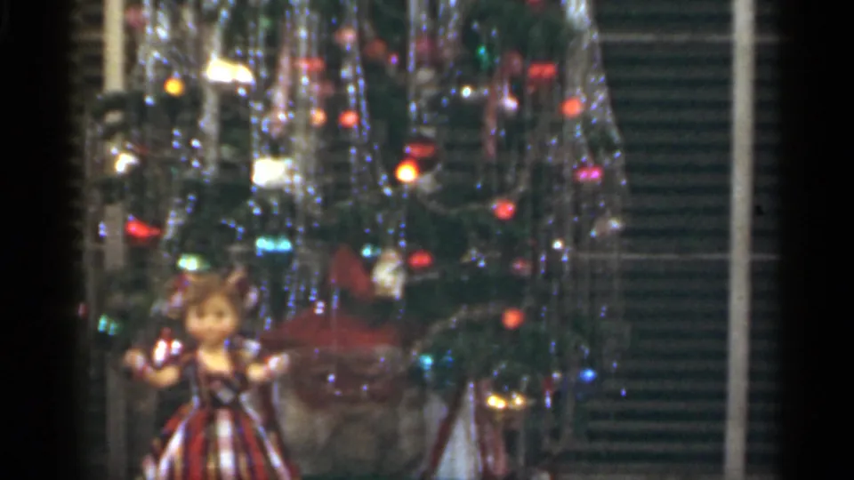 1949 Santa Cruz home-movie frame showing the lower Christmas tree with a plaid-dress doll and wrapped gifts near the base.