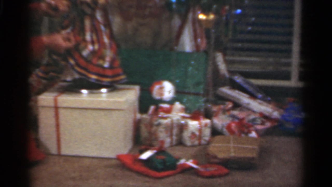 Christmas gifts, a small doll, tinsel, and a large wrapped box sit under the tree in a Santa Cruz domestic interior.