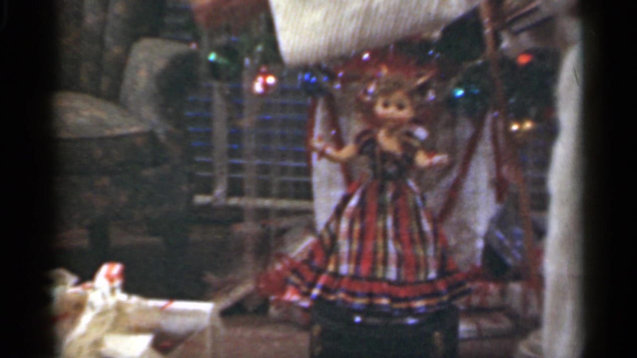 Plaid-dressed doll near a decorated Christmas tree with wrapping paper in a living room.