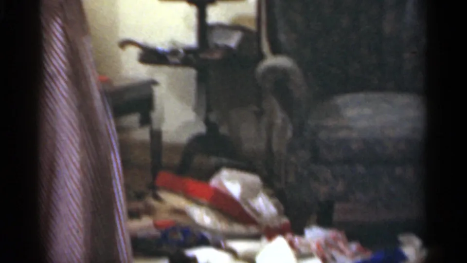 A partially framed adult stands near furniture and Christmas gift wrap in the 1949 Santa Cruz home-movie interior.