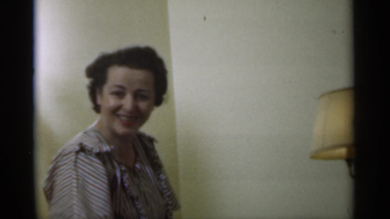Adult woman smiling toward the camera beside a shaded wall lamp.